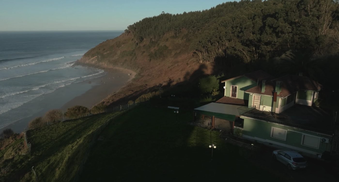 La casa: verde, en la ladera sobre la playa, con el mar y las olas a la izquierda